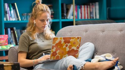 A student reclines on a sofa, working on her laptop