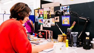 Falmouth University Illustration student wearing a red jumper and drawing at a desk