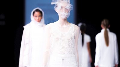 Models on a catwalk wearing white clothing and a netted face mask