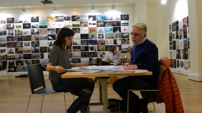 A student and lecturer sat at a table with a photo montage on the wall