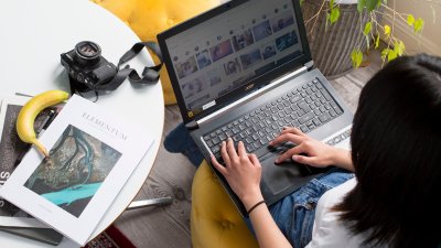 A student working on a laptop next to a white table with a camera and magazine