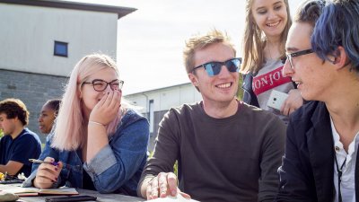 Students sat at bench outside with sunglasses and smiling.