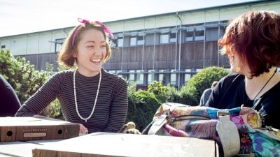 Student smiling with pink head scarf and pizza boxes on table.