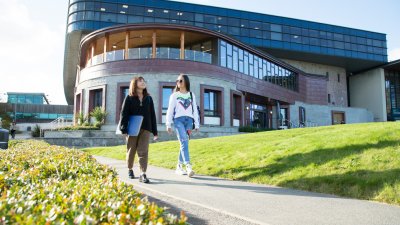Two students walking past a large building on Penryn Campus