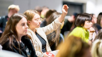 Female student raising hand in a crowd