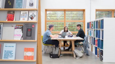 Three students sat at a table in a Graphic Design studio at Falmouth University