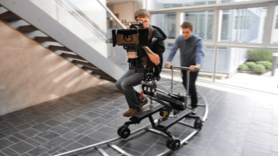 Student behind camera on camera dolly being moved along a track.