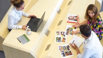 Two women and a man seated at a desk with a laptop and print outs