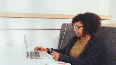 Female student seated at white table with laptop and open notepad