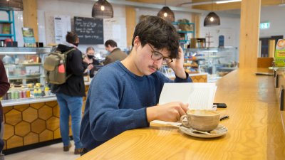 A student reading at a table in the cafe on Penryn Campus