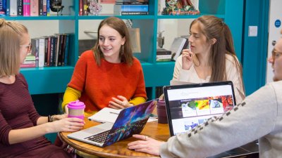 Four Falmouth University students talking at a table in front of bookshelves.