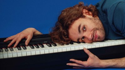 A person laying on top of a piano keyboard against a royal blue backdrop