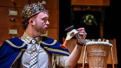 A person on stage performing wearing a crown and using a puppet duck