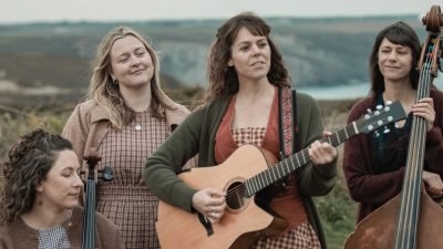 4 musicians holding instruments set against the rugged Cornish cliffs