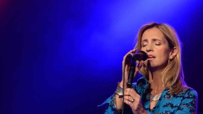 A person stood on stage under lighting singing into a handheld microphone