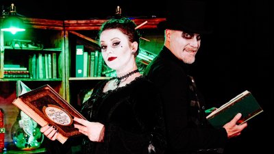 Two performers dressed in gothic costumes holding books and looking at the camera