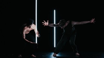 Two dancers on stage in very dim light performing around two white strip lights