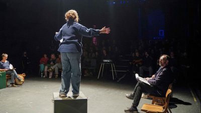 Performer with their back to the camera on stage under a spotlight performing to an audience