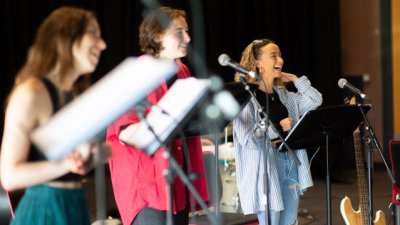 Three performers holding sheet music singing into microphones on stage