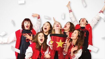 A group of performers posing in red outfits on a white background on top of the Notflix logo