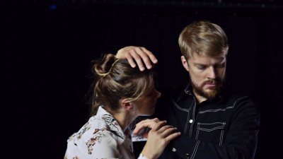 Two performers dancing on in close contact against a dark black backdrop