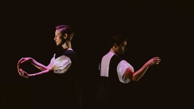 Two dancers wearing black and white costumes dancing against a black background