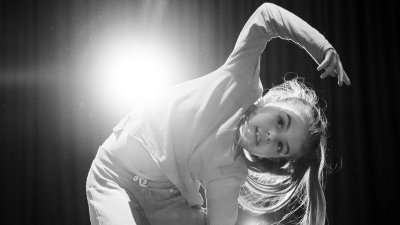 A black and white image of a young dance posing for the camera with a bright light in the background