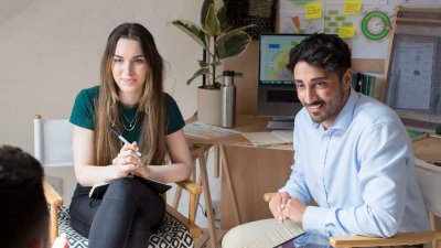 Three people seated in conversation with graphs and a plant in the background