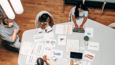 Birds eye view of group of people sat around a table with business strategy papers