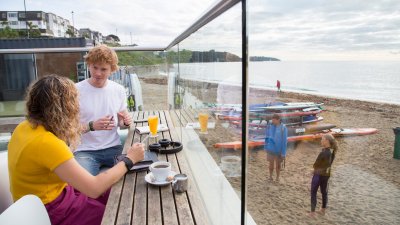 Falmouth University students sat on the terrace at Gylly Beach Cafe with the sea in the background
