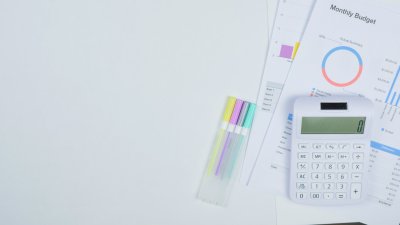 A white calculator and pens next to paper with financial graphs