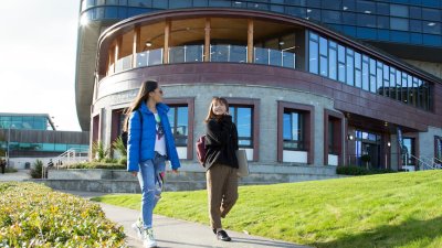 Two female students walking along a path with a large building in the background