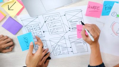 hands sketching a sitemap with a laptop and coloured post-it notes on a table
