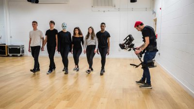 6 people walking in a line in a studio filmed by a lone cameraman 