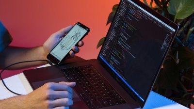 A laptop with code on the screen is connected to a phone with an app open. 
