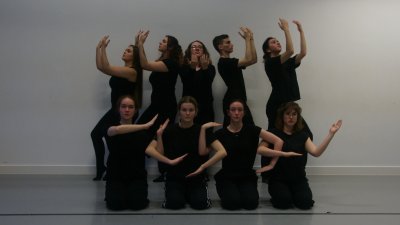 Nine dancers posing against a grey wall