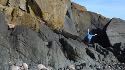 A distance image of a solo dancers on the beach near a rocky cliff