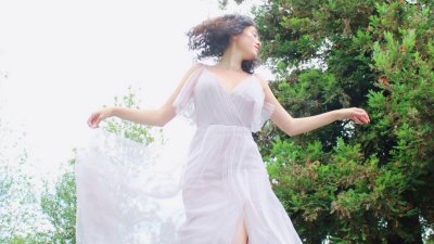 A solo female in a white dress that is moving in the wind in front of a tree