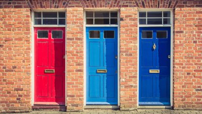 A row of 3 colourful front doors on a brick building