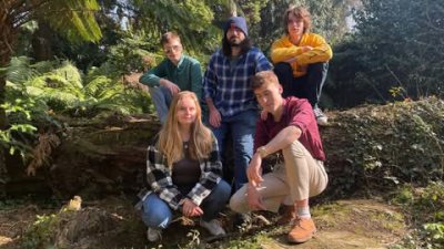5 people sat on the floor in front of a tree trunk