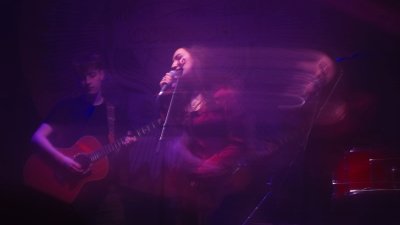 A photo of people performing which is slightly blurred with pink and purple lighting