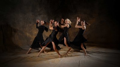 4 female dancers posing on a staged background wearing all black