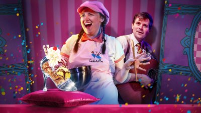 A performers in an ice cream booth with an ice cream sundae in a glass slipper in the front of the image