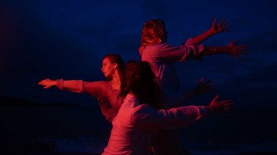 A dark and moody image of 3 dancers performing outside with a red light on them
