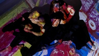 Dancers on stage with a projection of a multi coloured painting overlayed on them