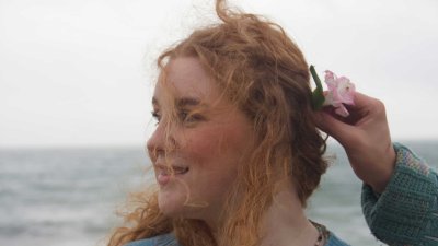 a person looking to the right wearing a blue jumper on a black with a flower being held in their hair