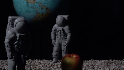 A globe with two plastic figurines and an apple in the front of the image