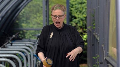 A performer located in a bike shed wearing black clothing holding a wireless speaker