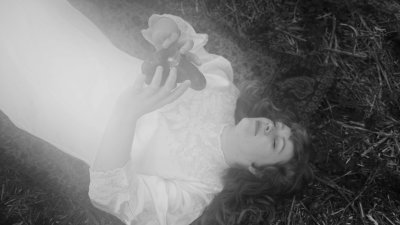 A black and white image of a person laying on the floor in a white dress holding an object
