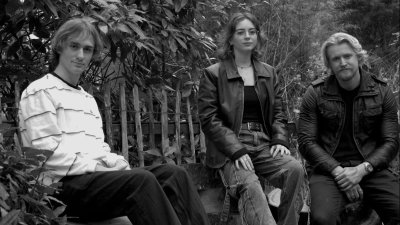 A black and white image of three musicians sat on a bench in a line.